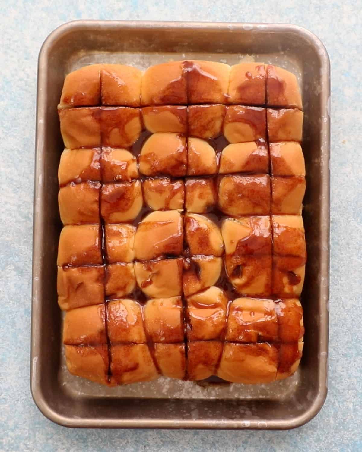brown syrup topped Hawaiian rolls in a metal sheet pan.