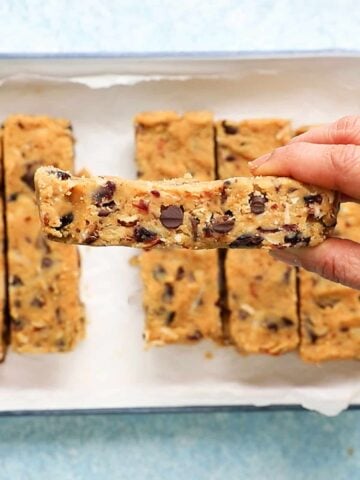 a hand holding one almond bar above a white tray filled with more.