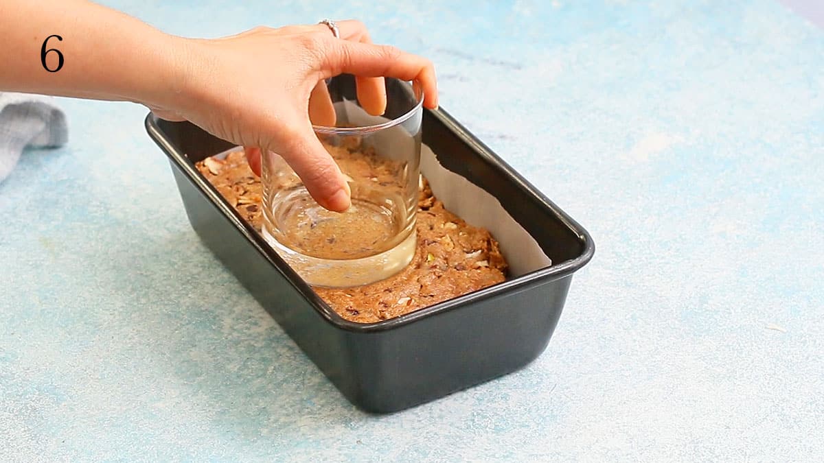 a hand pressing almond dough in a loaf pan using a glass.