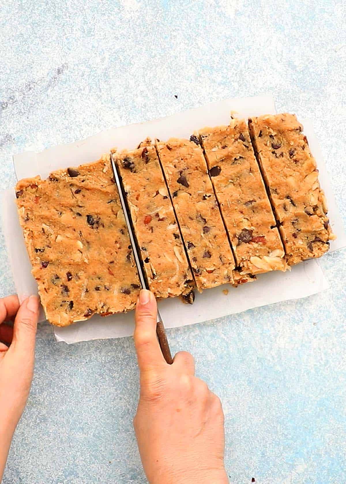 two hands cutting almond bars dough into bars.