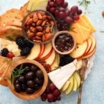 sliced cheeses, fruits and nuts arranged on a white marble board.