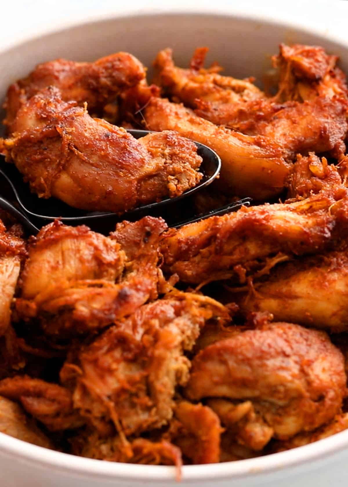 chunks of red colored chicken in a white plate along with black spoon.