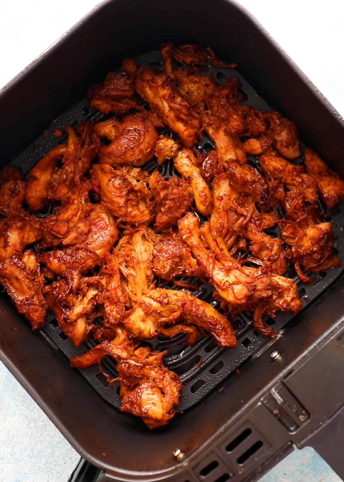 red chunks of chicken shawarma in an black air fryer basket.