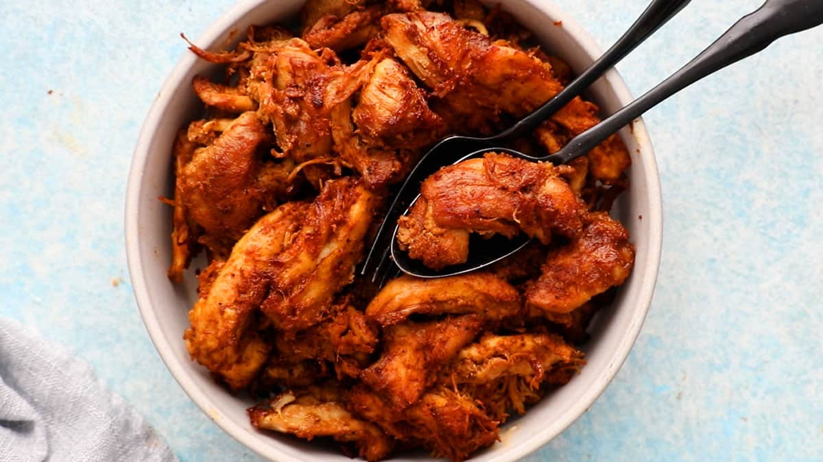 chunks of red colored chicken in a white plate along with black spoons.