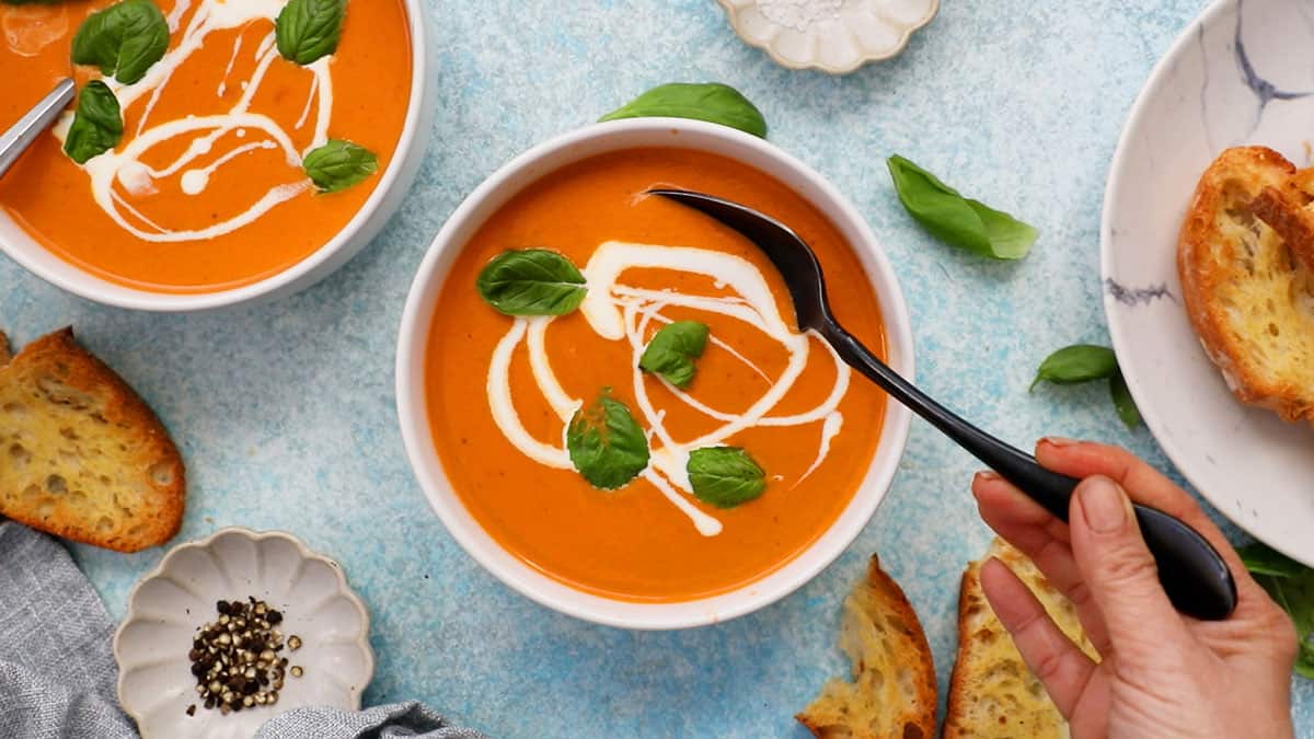 orange colored tomato soup in two white bowls along with a black spoon.