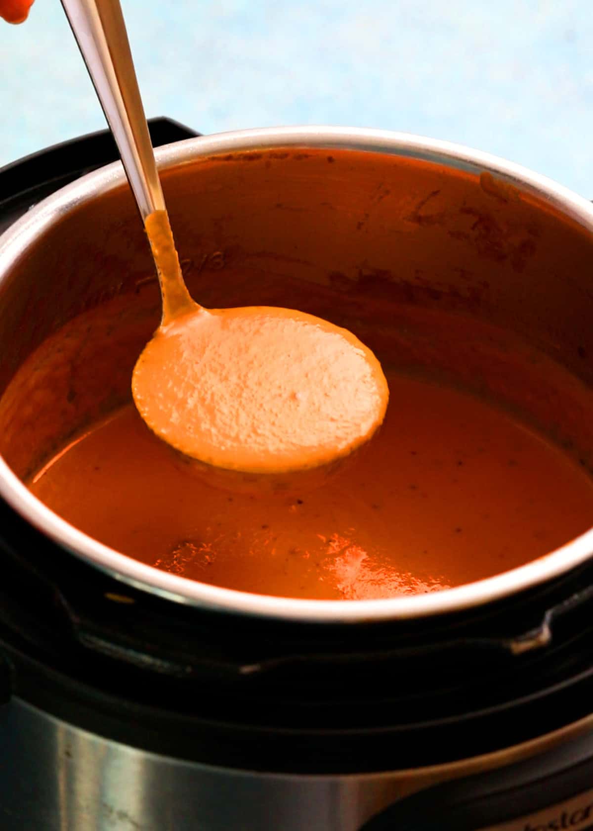 one ladle full of orange tomato soup above an instant pot.