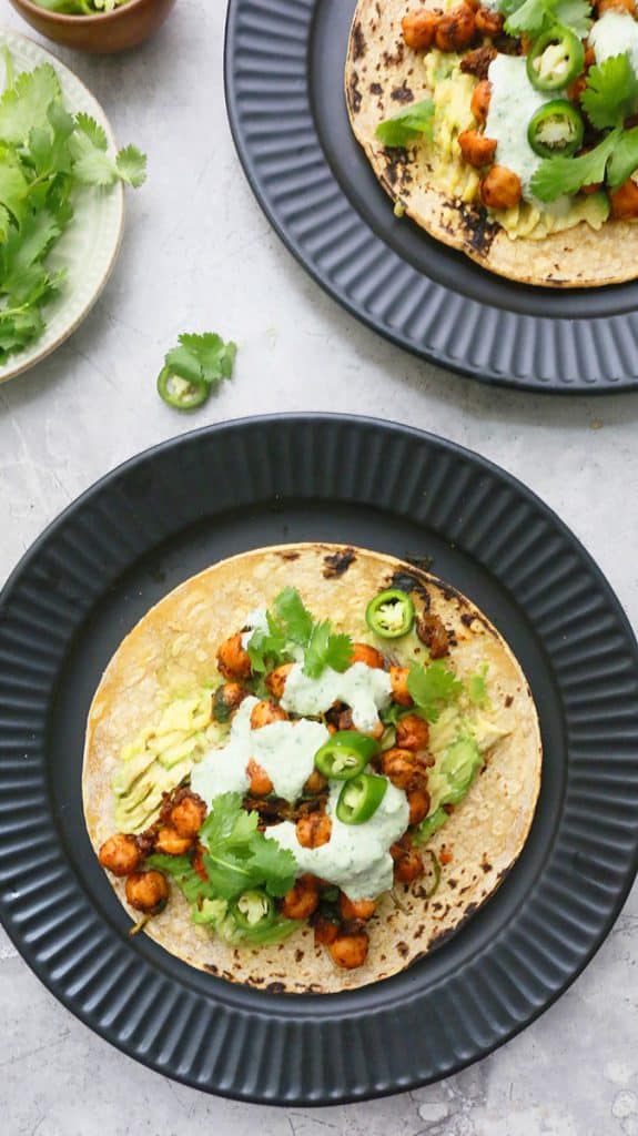 black plates with assembled tacos and cilantro on the side