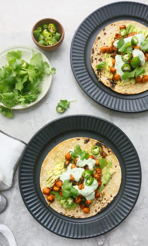 black plates with assembled tacos and cilantro on the side