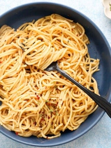 cooked spaghetti noodles along with one black fork in a large blue bowl.