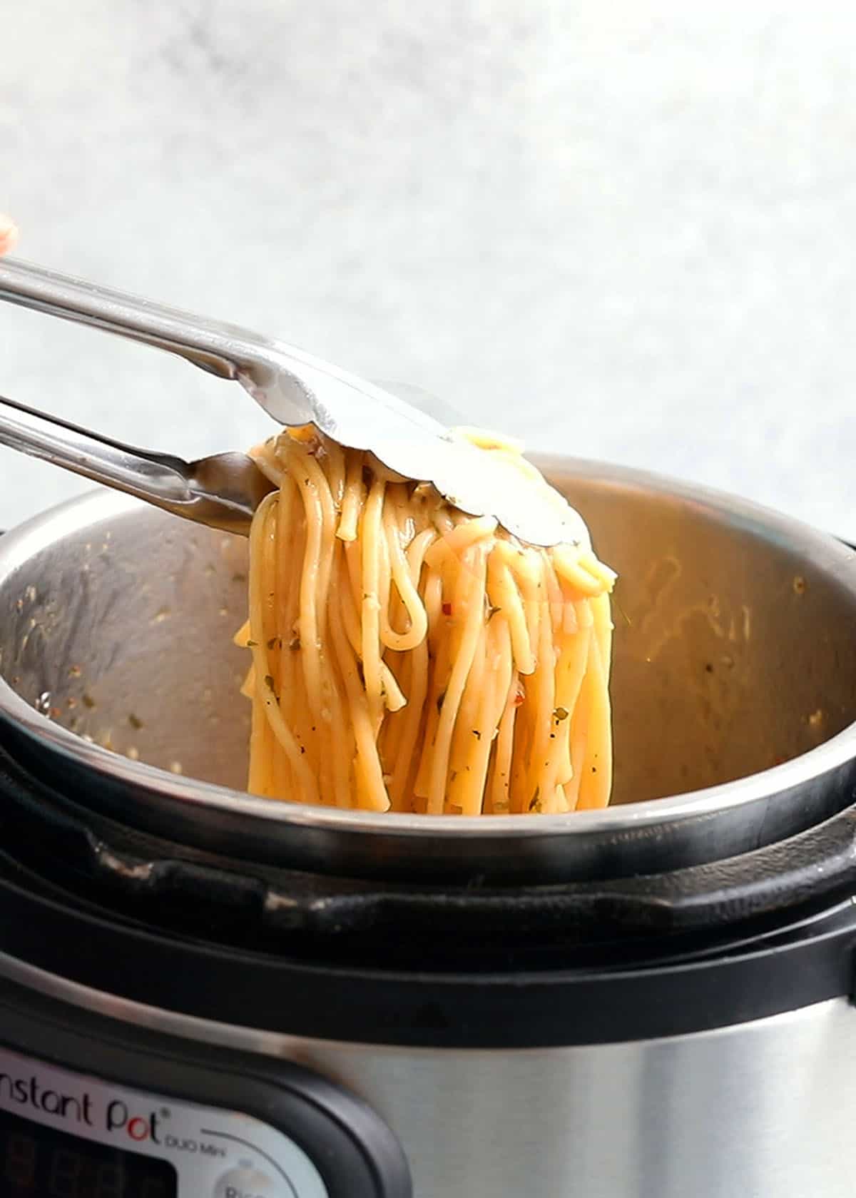 a hand lifting cooked spaghetti using tongs from an instant pot.