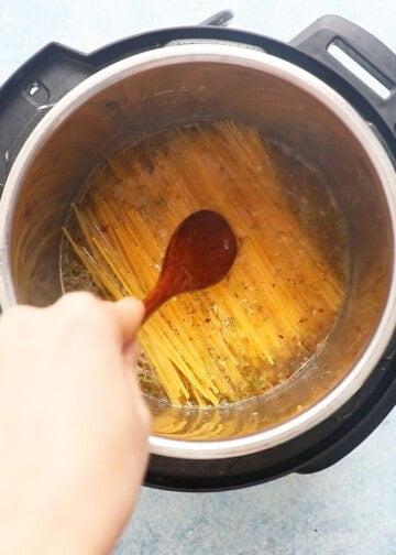 a hand mixing spaghetti with water in an instant pot.