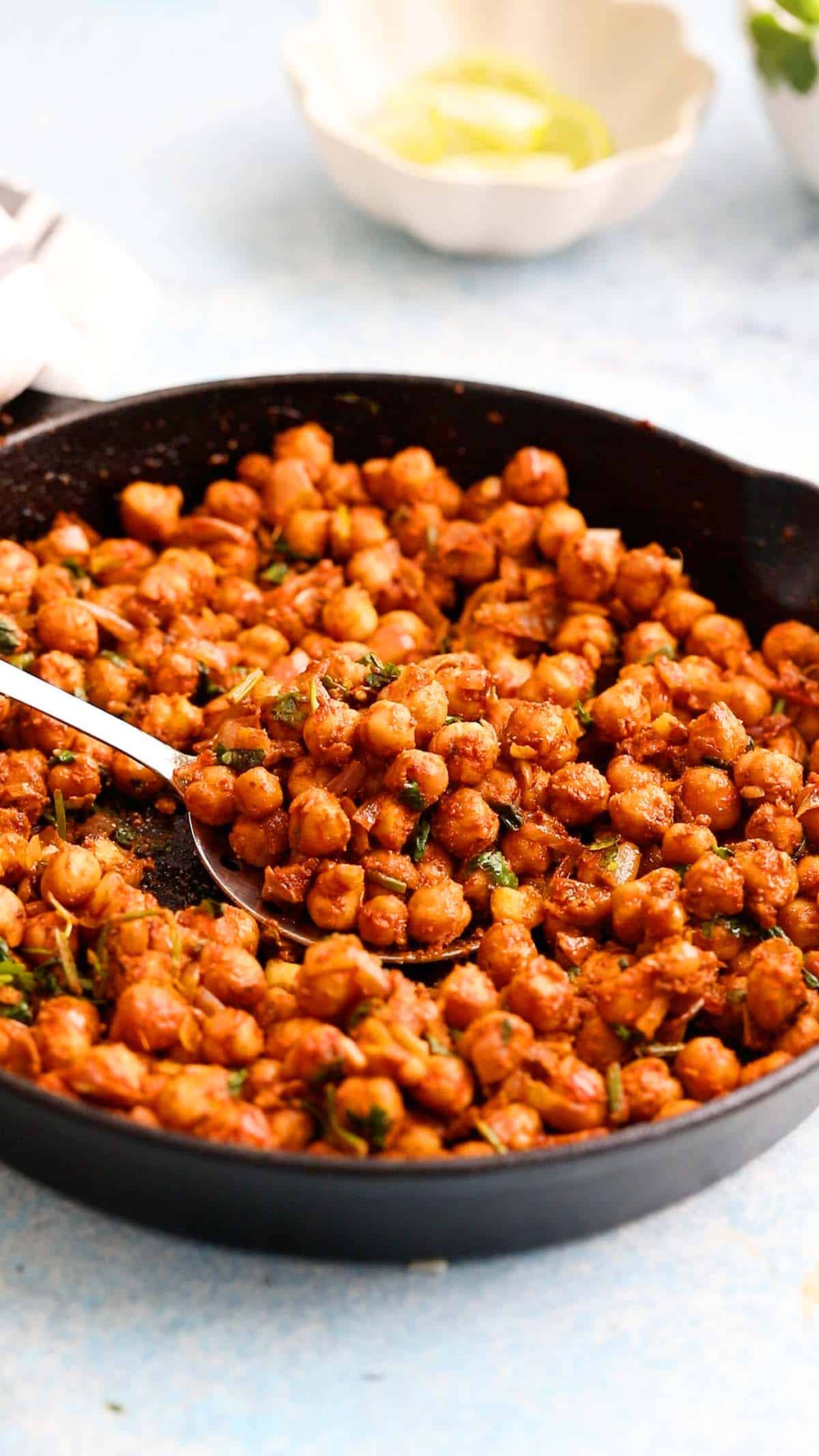 cooked spicy chickpeas in a black skillet along with a spoon.