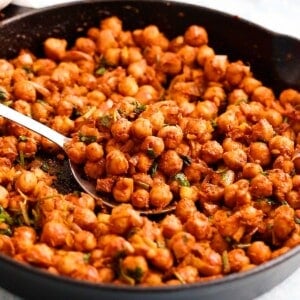 cooked spicy chickpeas in a black skillet along with a spoon.