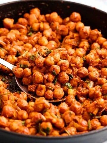 cooked spicy chickpeas in a black skillet along with a spoon.