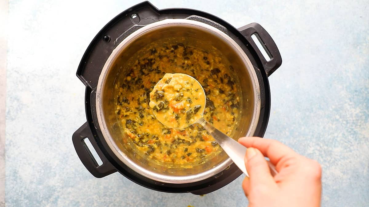 a ladle full of yellow dal above an instant pot filled the same.