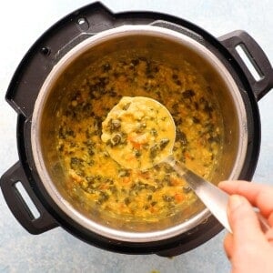 a hand holding one ladle full of dal above an instant pot.