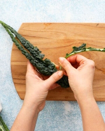 two hands removing the centre rib from one kale leaf.