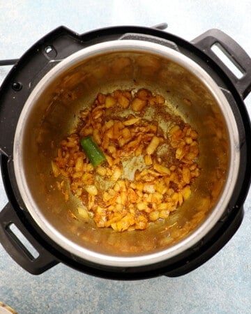 an instant pot with chopped onion and spices cooking in oil.