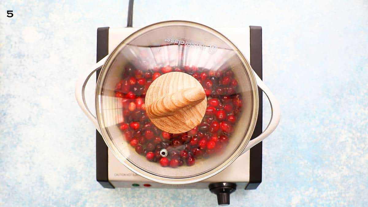 a covered white saucepan with cranberry sauce placed on the stovetop.