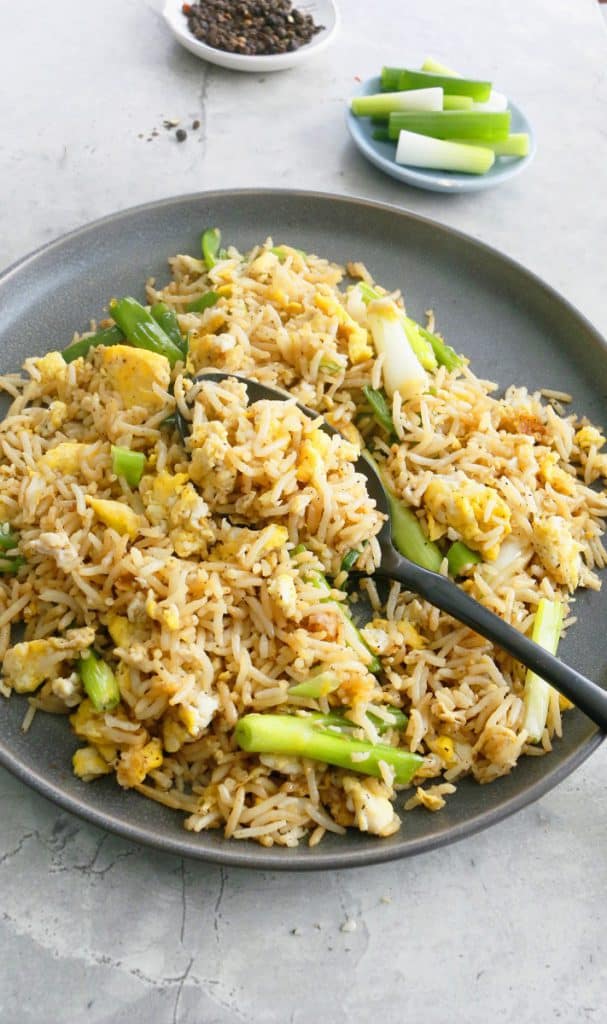 a grey plate with cooked egg, rice and scallions with a black spoon 