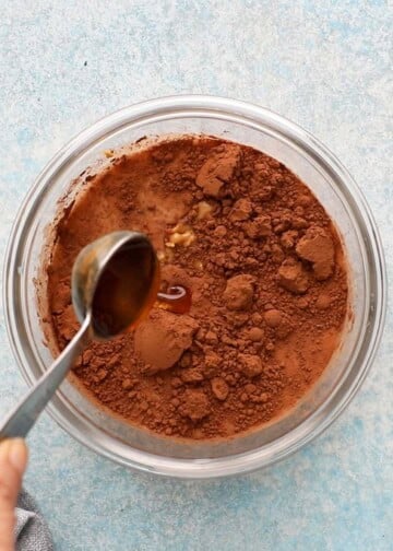 a hand adding honey into a glass bowl with brown liquid.