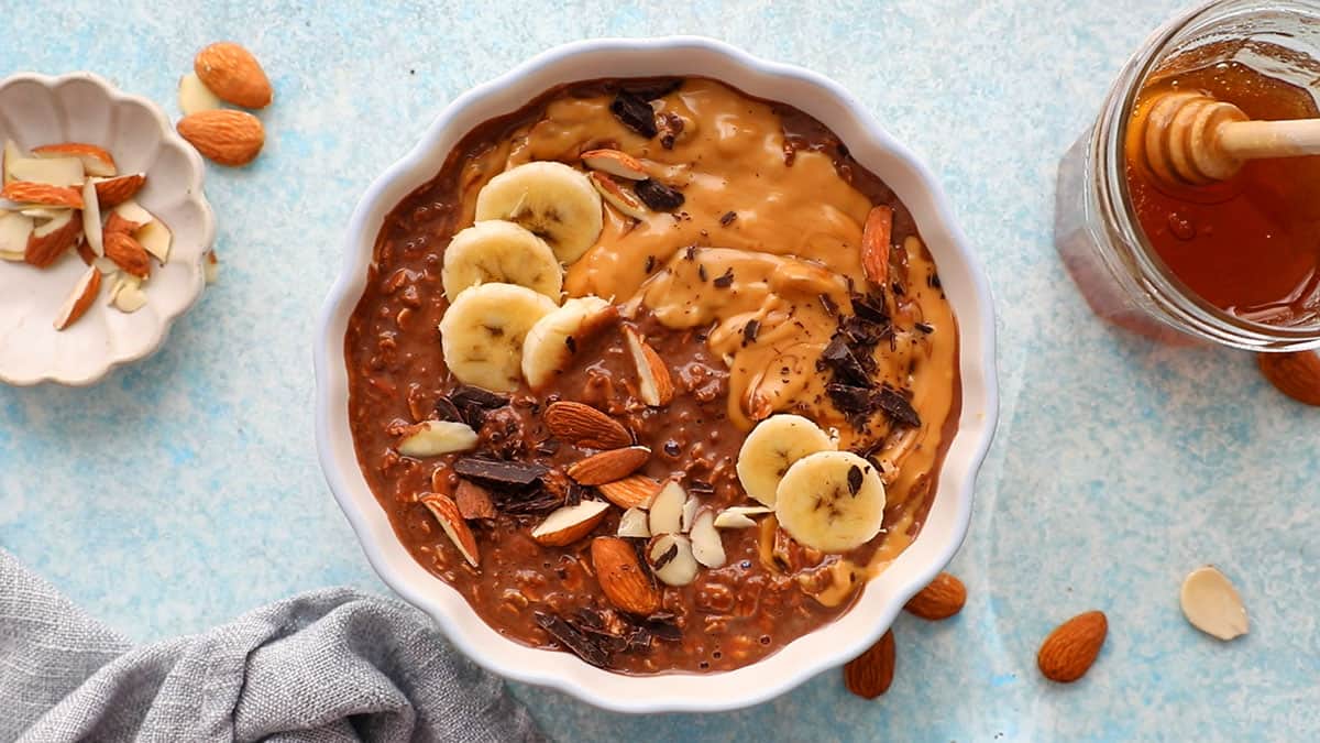 brown chocolate overnight oats in a white scalloped bowl along with a spoon.