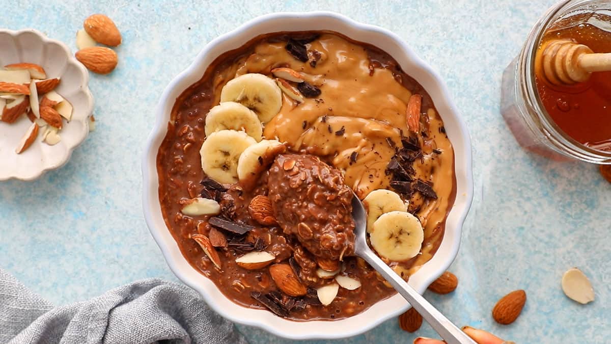 brown chocolate overnight oats in a white scalloped bowl along with a spoon.