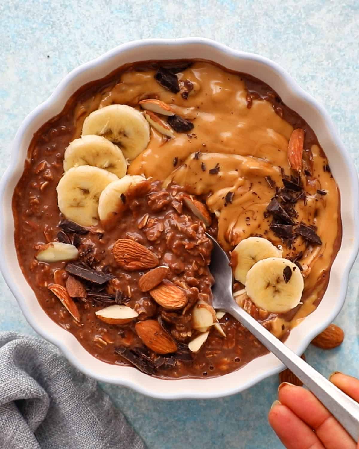 brown chocolate overnight oats in a white scalloped bowl along with a spoon.