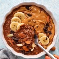 brown chocolate overnight oats in a white scalloped bowl along with a spoon.