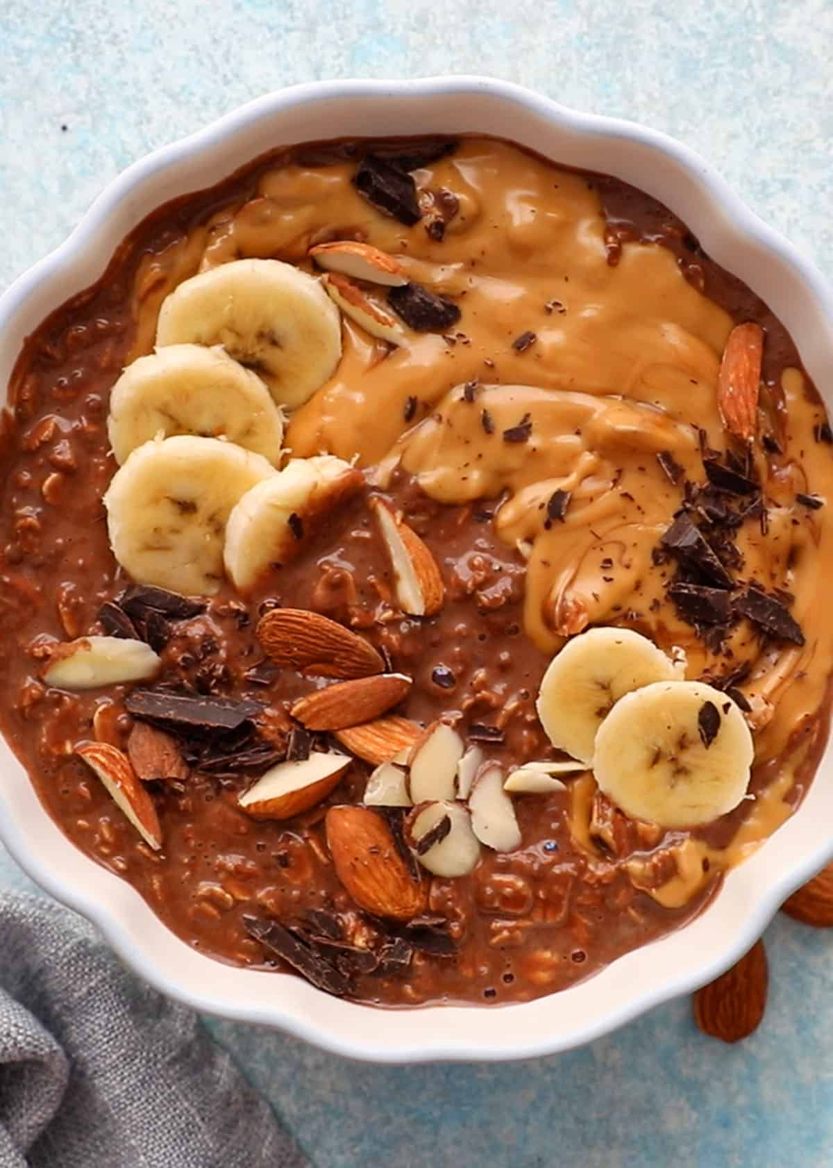 brown chocolate overnight oats in a white scalloped bowl along with a spoon.