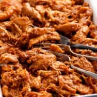 red colored bbq chicken in a white tray along with two forks.