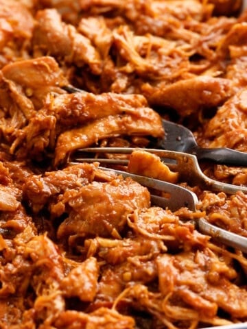 red colored bbq chicken in a white tray along with two forks.