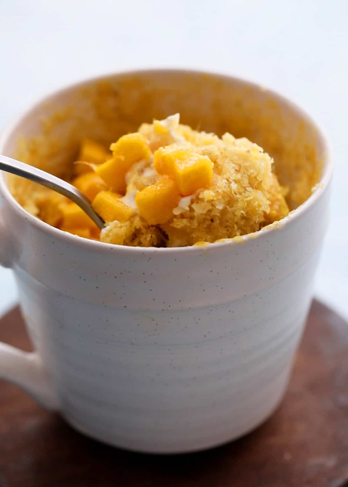 a spoonful of mango mug cake in a white mug.