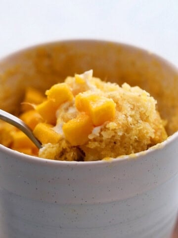 a spoonful of mango mug cake in a white mug.