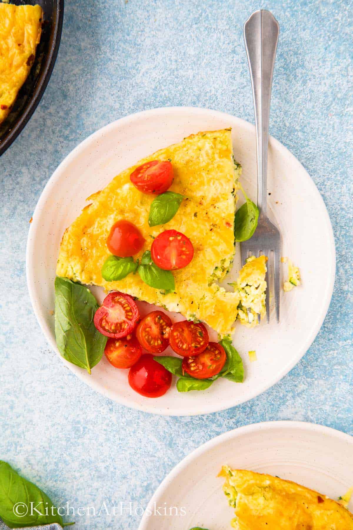 a slice of frittata on white round plate with tomatoes on the side.