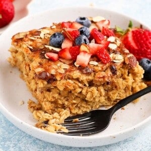 one square piece of baked oatmeal, topped with berries in a white bowl.