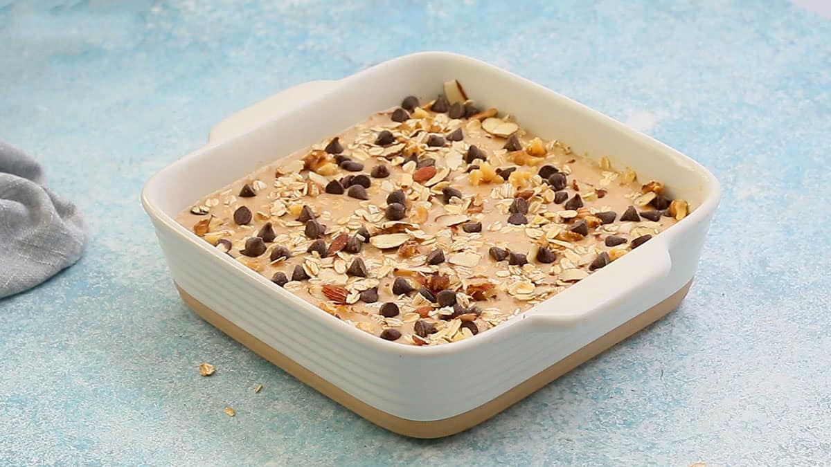 one white square baking pan with baked oatmeal mixture, topped with chocolate chips and nuts.