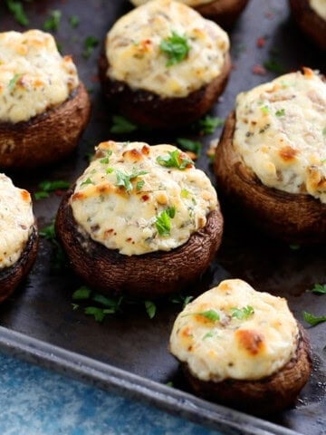 white cheese stuffed mushrooms placed on a black metal sheet.