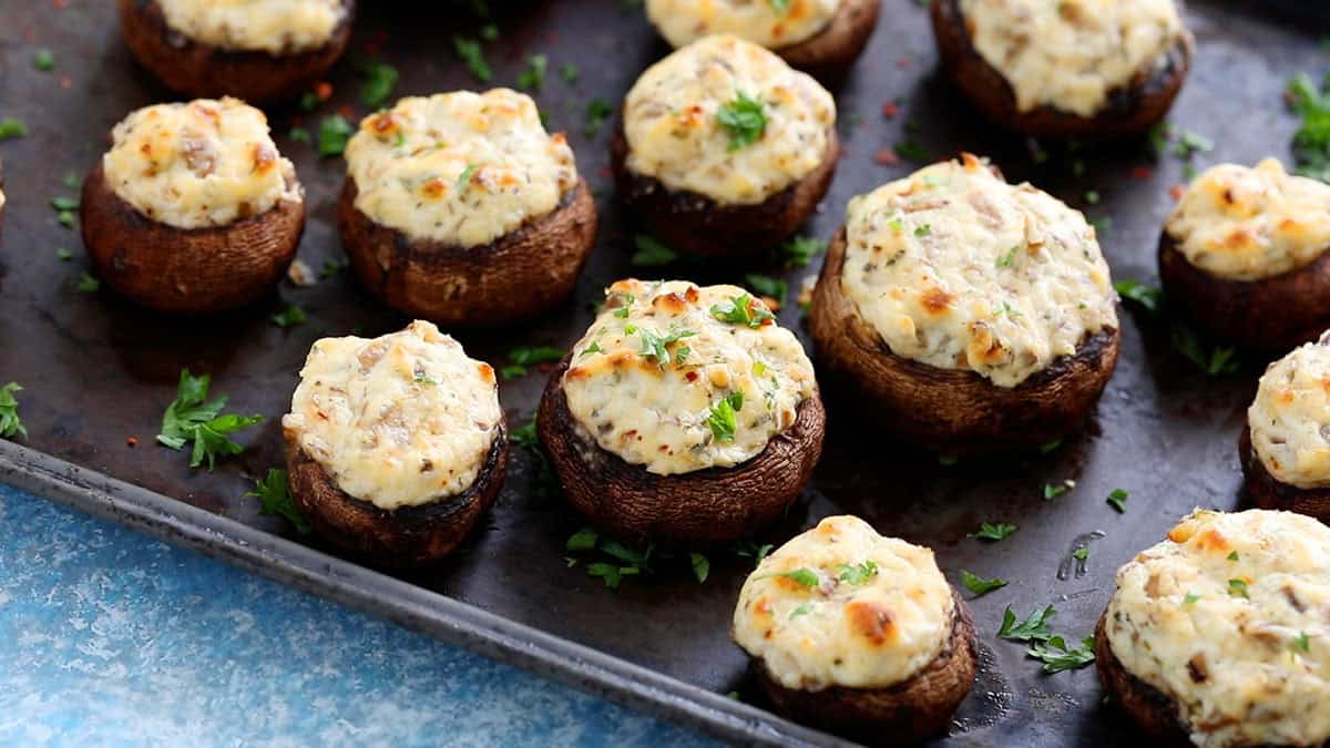 white cheese stuffed mushrooms placed on a black metal sheet.