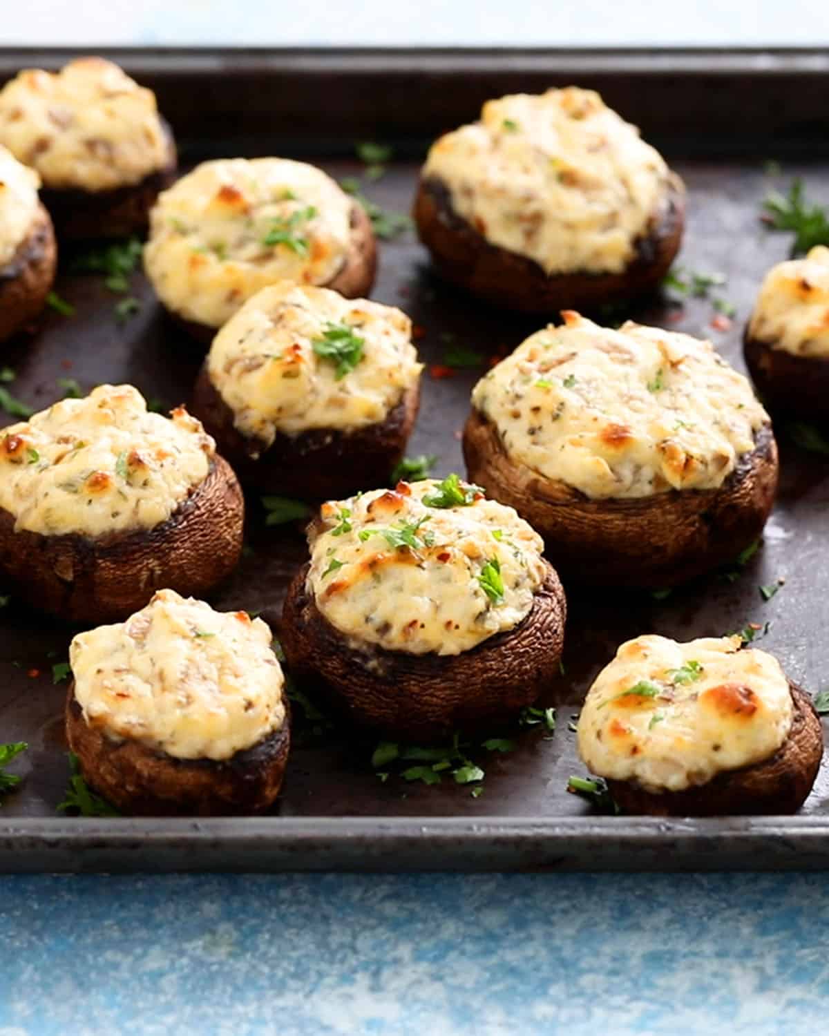 white cheese stuffed mushrooms placed on a black metal sheet.
