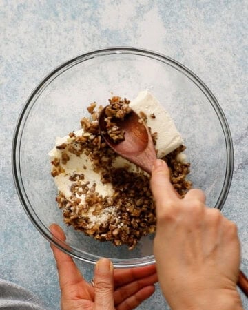 two hands mixing white cheese and mushroom stuffing in a large glass bowl.