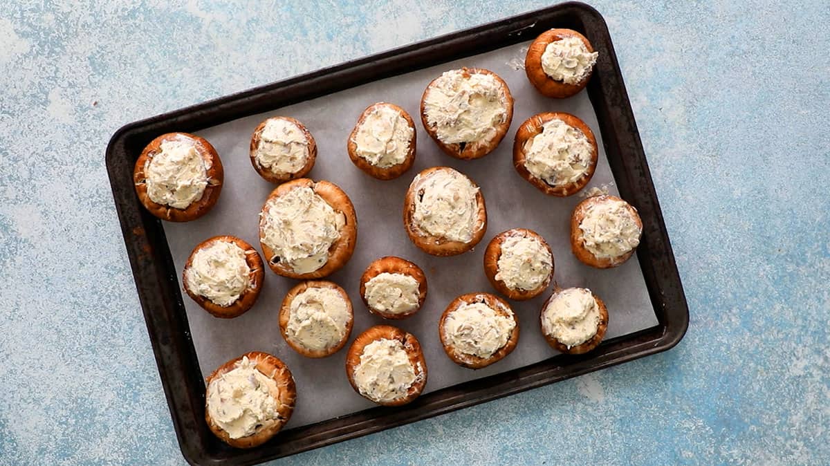 white cheese stuffed mushrooms placed on a black metal sheet.