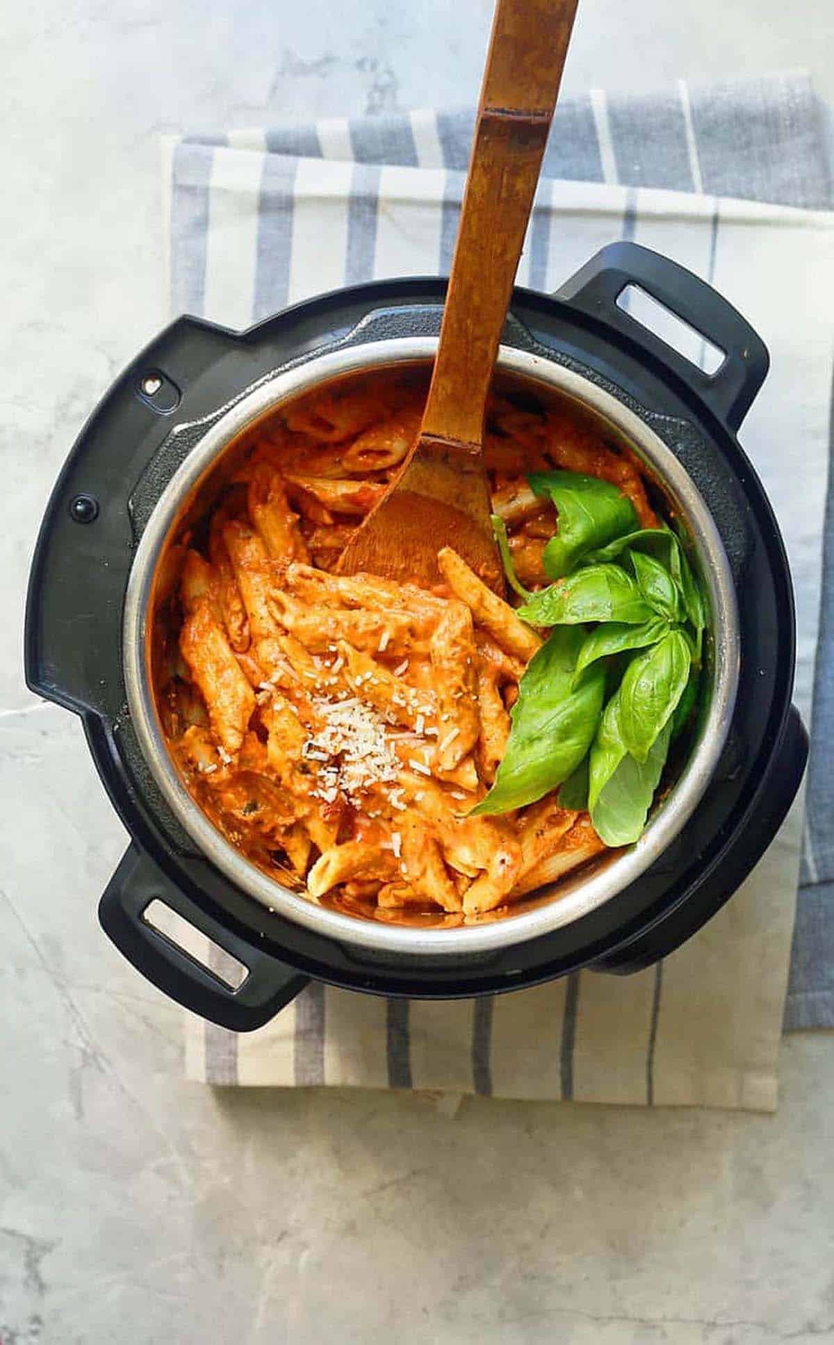 an instant pot filled with cooked pasta and garnished with fresh basil leaves.