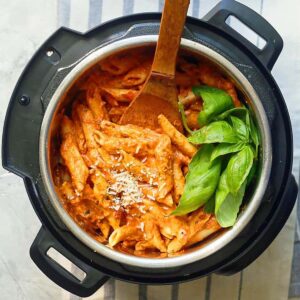 cooked tomato sauce pasta in instant pot, with fresh basil and wooden spoon.
