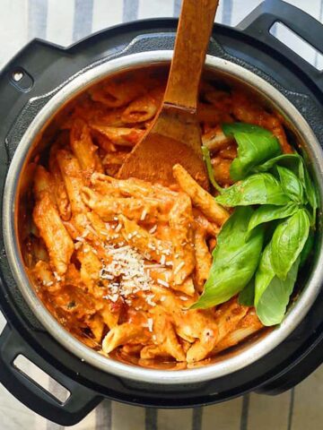 cooked tomato sauce pasta in instant pot, with fresh basil and wooden spoon.