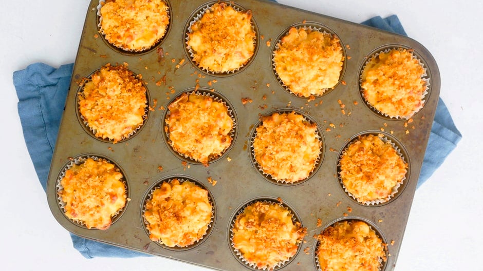 uma panela de muffin com macarrão e muffins de queijo arrefecendo num pano azul