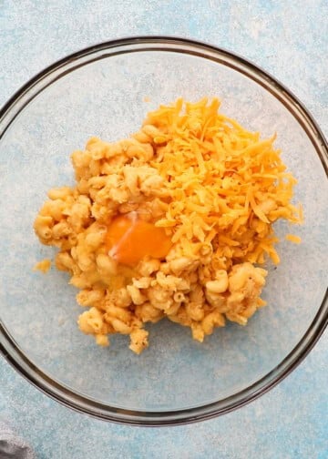 cooked macaroni and cheese, egg and yellow cheese in a glass bowl.