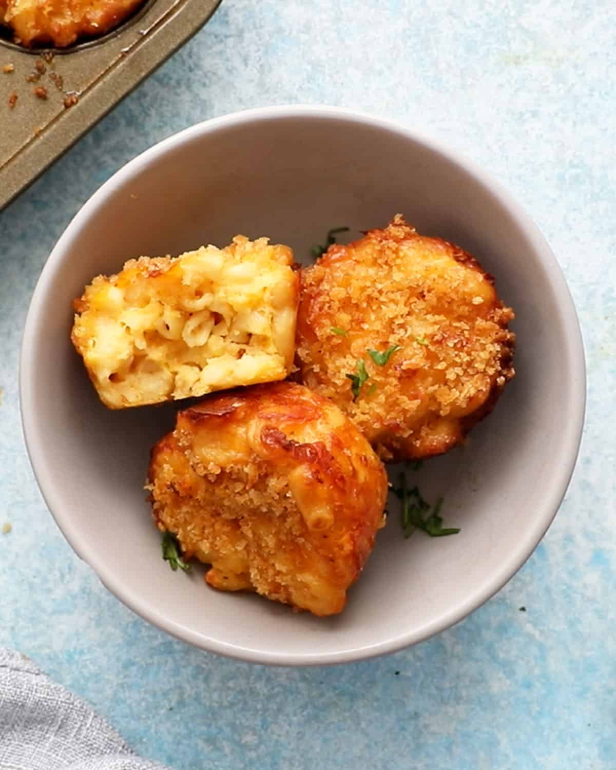 three baked macaroni and cheese muffins in a grey bowl.