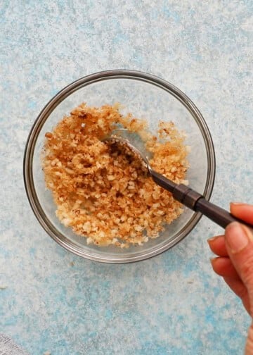 a hand mixing brown bread crumbs in a small glass bowl.