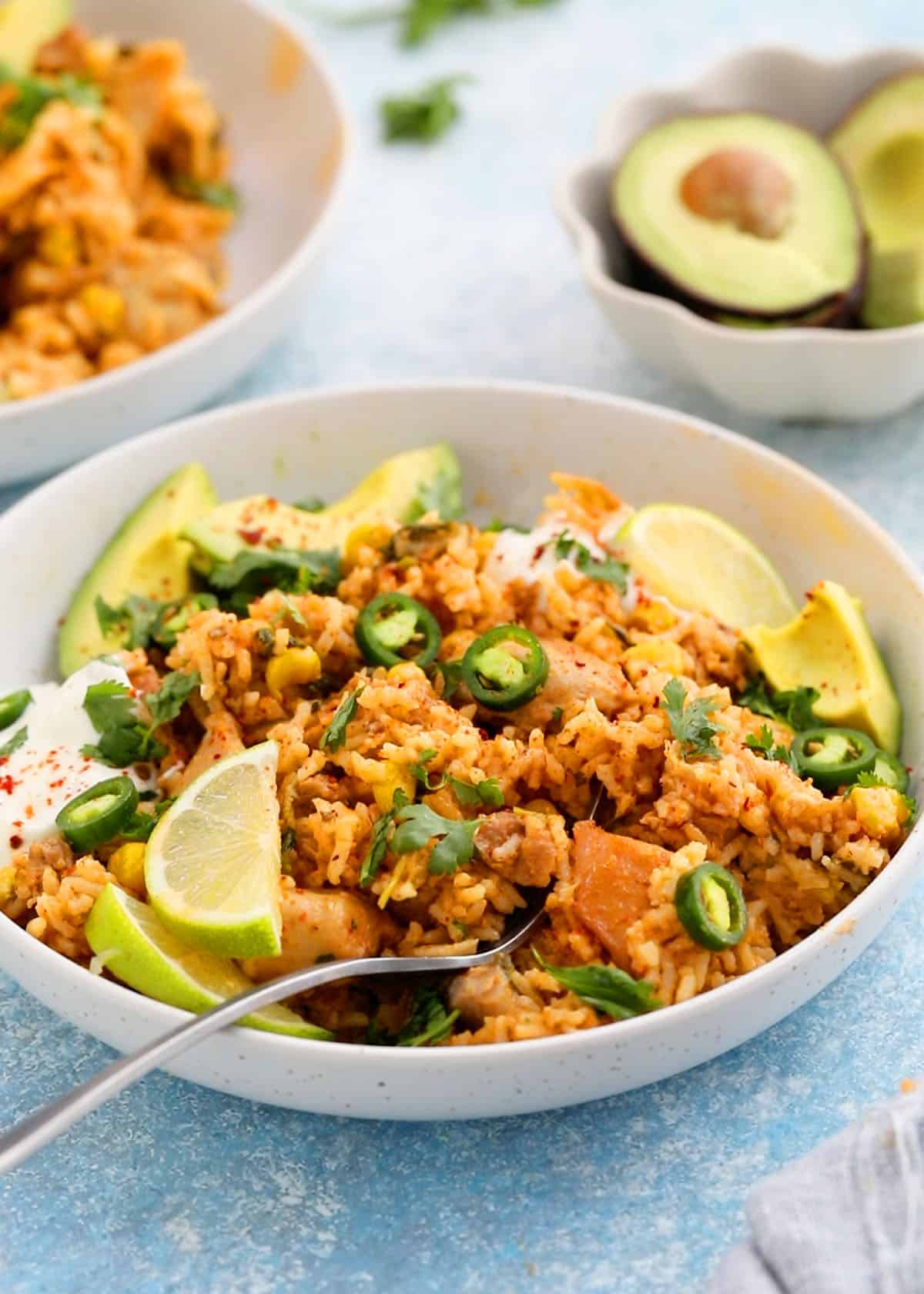 cooked chicken and rice in a white bowl topped with green peppers and avocado.